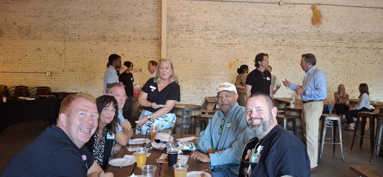 Attendees gathered around a long table with food and drinks at the launch meetup, with more people talking in the background.
