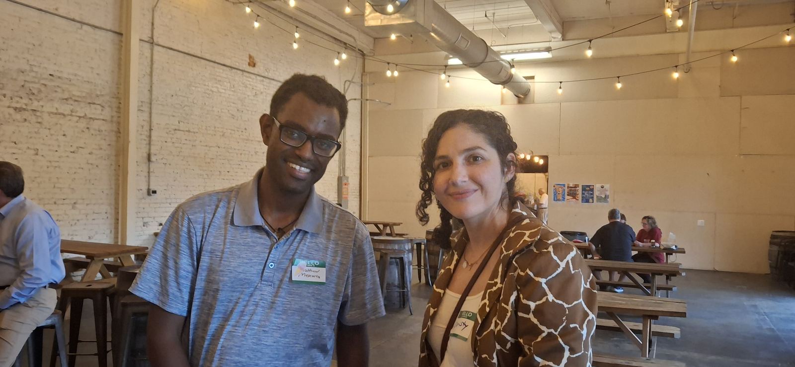 Two attendees wearing name tags, standing and talking in the brewery's main room.